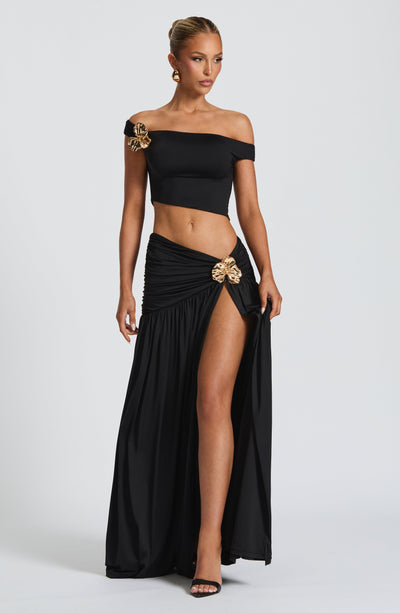 Conjunto negro de top fuera de hombros y falda larga con abertura lateral; broche dorado.